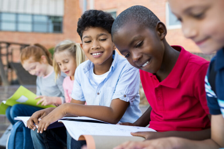 Multiethnic children sitting in a row and reading from notebook all together.